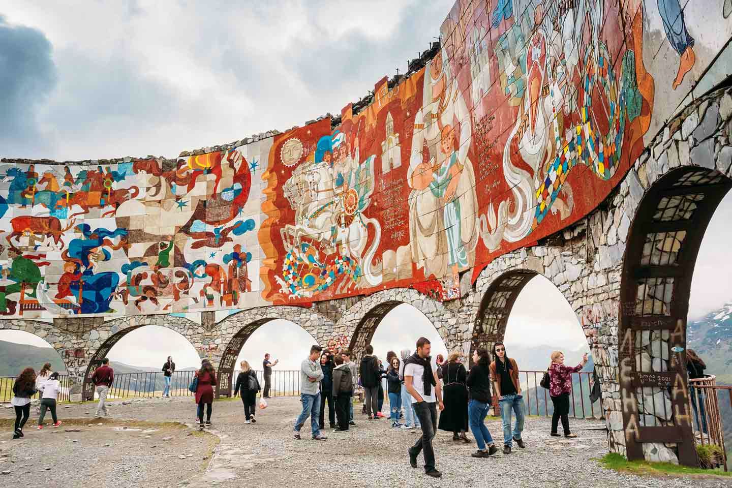 Tourists walking beneath historic stone arches decorated with colorful traditional Georgian murals and frescoes